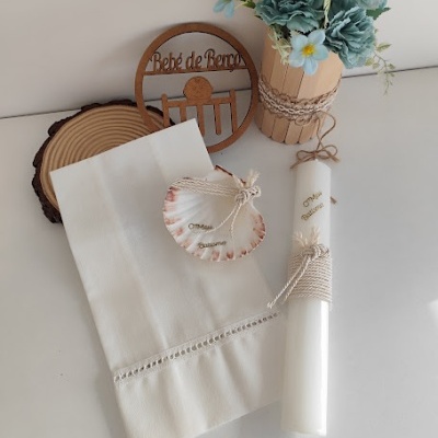 Conjunto decorativo com vela, toalha branca, concha, flores azuis e base de madeira