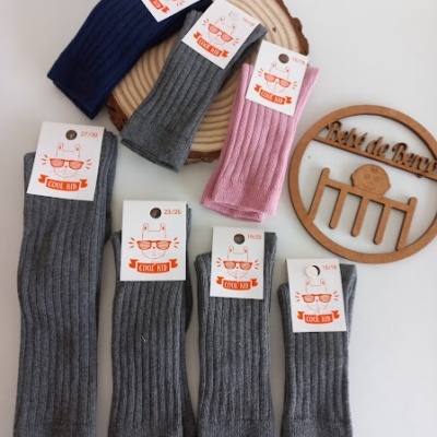 Sete pares de meias caneladas com etiquetas com desenho de gato e texto COOL KID sobre superfície branca e objeto de madeira