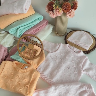Roupas de bebé em malha coloridas pastéis com padrões delicados e vaso com flores secas