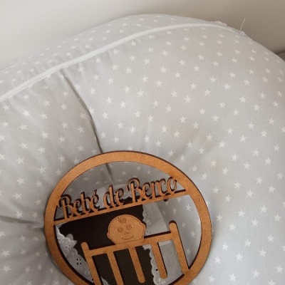 Almofada cinza com estrelas brancas e enfeite redondo de madeira com texto 'Rede de Berço'