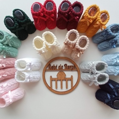 Sapatinhos de bebé de tricô em diversas cores dispostos em círculo com um símbolo de madeira no centro