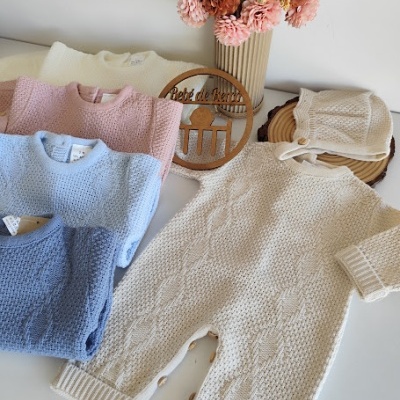 Roupas de bebé em malha de várias cores dispostas sobre uma mesa branca com flores decorativas