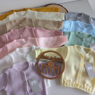 Oito casacos de malha de bebé em várias cores claras com botões e etiquetas.