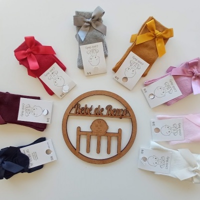 Collants para bebé coloridos com laços e etiquetas dispostos em círculo com um emblema de madeira ao centro