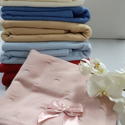 Cobertores de malha empilhados com laço rosa e flor branca ao lado