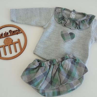 Conjunto de roupa de bebé com camisola cinzenta e saia xadrez em tons verde e cinza sobre fundo branco.