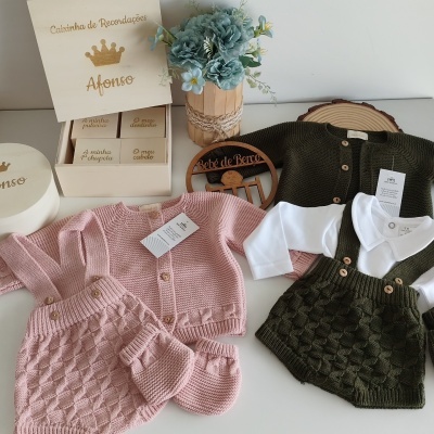 Roupas de bebé em tricô rosa e verde com caixa de recordações e vasos de flores azuis