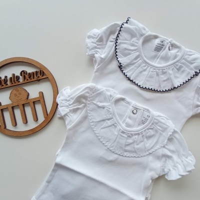 Dois bodies brancos para bebé com golas frisadas e placa de madeira com texto e imagem de berço