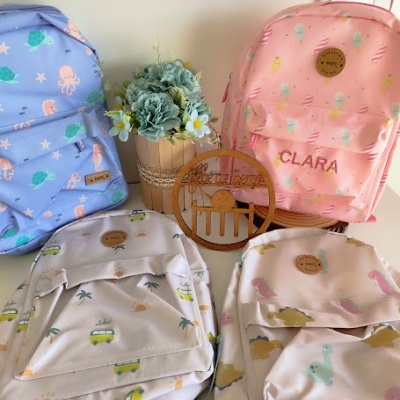 Quatro mochilas infantis coloridas com padrões e nome CLARA, vaso com flores e ornamento de madeira