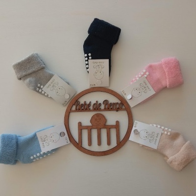 Cinco pares de meias antiderrapantes para bebé em várias cores em volta de um círculo de madeira com texto