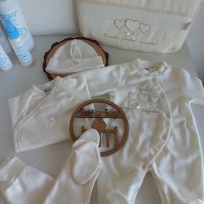 Conjunto de roupa de bebé cru com bordados bege e embalagens de produtos de cuidado