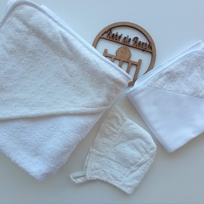 Três toalhas brancas com detalhes em relevo e uma placa de madeira redonda com texto e ícones gravados.