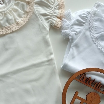 Dois bodies infantis, um creme com rendas bege e outro branco com rendas brancas, com círculo decorativo de madeira.
