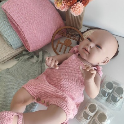 Boneca com fato e sapatos cor-de-rosa de malha junto a mantas e flores