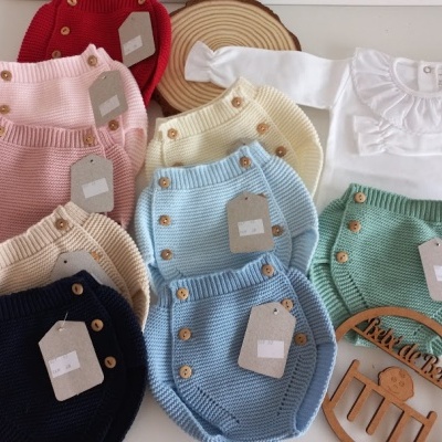 Conjunto colorido de roupas de bebé em malha e body branco com golinha, etiquetas penduradas, boneco de madeira Kids & Beans