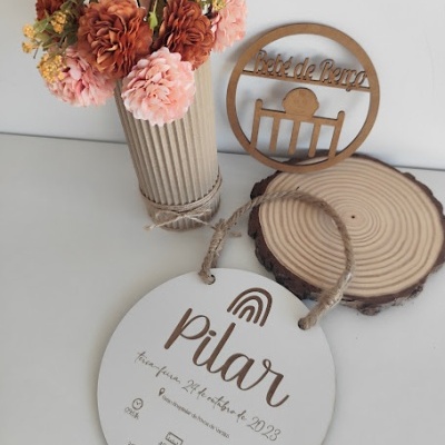 Placa redonda branca em madeira com texto Pilar, vaso com flores e decoração em madeira
