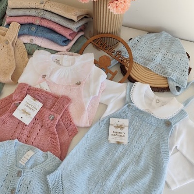 Roupas de bebé em malha azul e cor-de-rosa com golas brancas, boné azul e flores secas