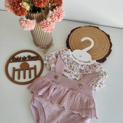 Roupa de bebé floral com saia rosa, vaso com flores e objetos decorativos em madeira