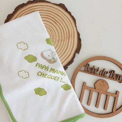 Fralda branca com bordas verdes e estampa de ursinho e nuvens verdes com texto 'PAPÁ MAMÃ CHEGUEI!...' e ornamento de madeira 'Bebé de Banho'