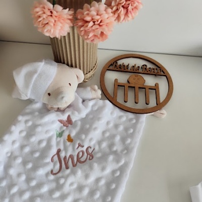 Boneco de peluche com tecido branco bordado com nome e sinal de madeira com texto