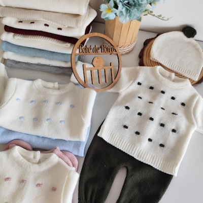 Conjunto de roupa de bebé com camisolas de malha e calças, placa de madeira Bebé de Reyes e vaso com flores