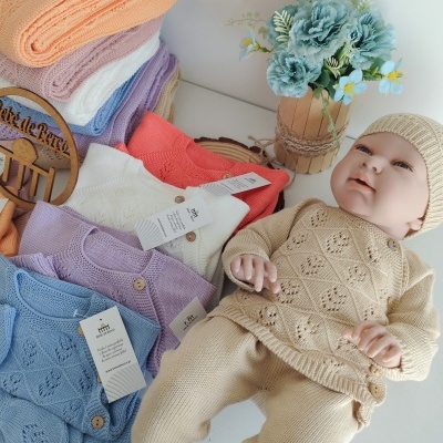Conjuntos de roupa de bebé em malha de várias cores com padrão trabalhado, boneco vestido de creme e vaso com flores azuis