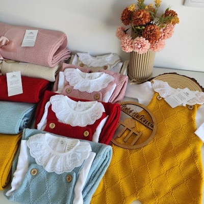 roupa de bebé em malha colorida com body branco e gola rendada, mantas e flores em vaso ao fundo