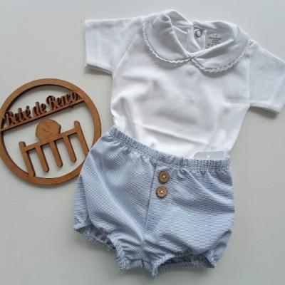 Conjunto de roupa para bebé com t-shirt branca e calções azuis às riscas, perto de placa de madeira com texto