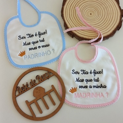 Babetes de bebé azul e rosa com texto em português e peça decorativa de madeira