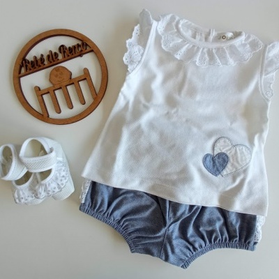 Conjunto de roupa de bebé com top branco, calções azuis e sapatinhos brancos, decorado com ícone de madeira