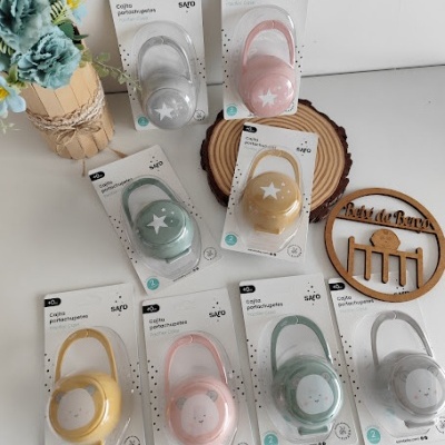 Capas porta-chupetas coloridas em embalagens sobre mesa com flores e decoração de madeira