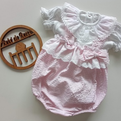 Body infantil rosa e branco com renda e laço, decoração de madeira redonda ao lado