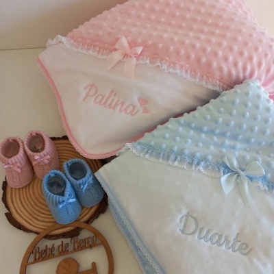 Mantinhos de bebé rosa e azul claro, com sapatinhos combinando e sinal de madeira com texto Bebé de Franco.