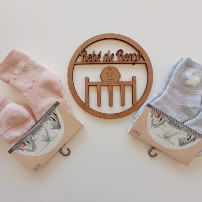 Dois pares de meias de bebé em rosa e azul claro com padrões, e enfeite de madeira com texto Bebé de Ferro