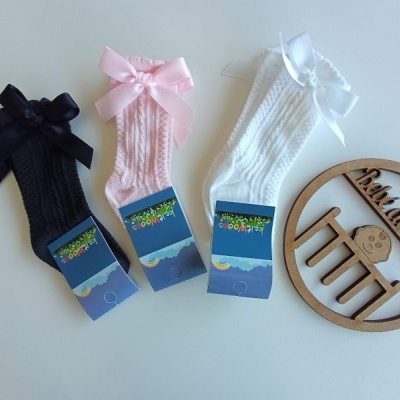 Três pares de meias para bebés com laço e etiqueta azul, ao lado placa redonda de madeira com frase e desenho