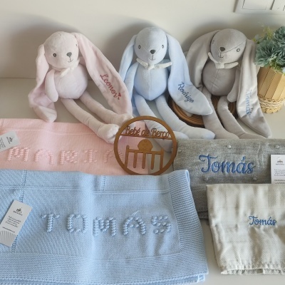 Três peluches coelho com mantas de malha bordadas com nomes.