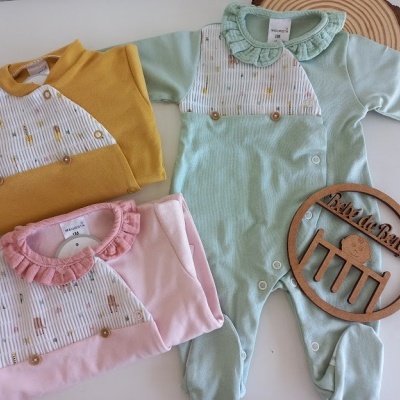 Três macacões de bebé coloridos com padrões e placa de madeira com texto