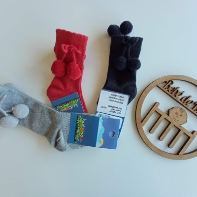 Três pares de meias com pompons e uma placa de madeira com texto