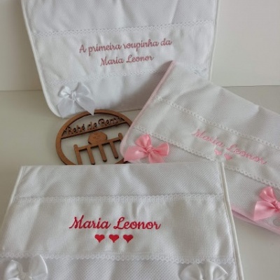 Três toalhas brancas bordadas com nomes e laços em cetim em superfície clara