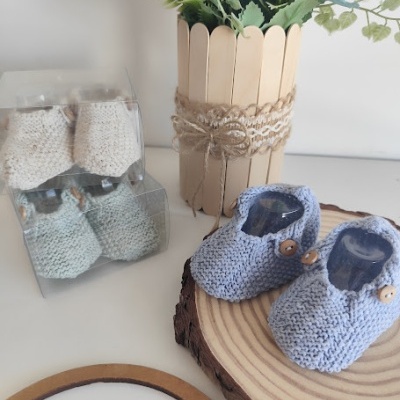 Chinelos de bebê em lã azul com botões, base de madeira e chinelos em caixas transparentes