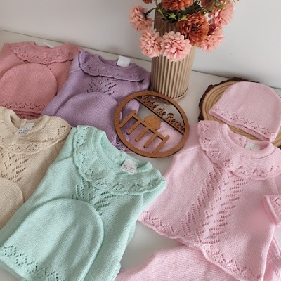 Conjunto de roupa de bebé em malha com padrões delicados em várias cores pastel, com flores em vaso ao fundo