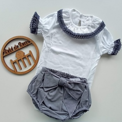 Conjunto de roupa de bebé com t-shirt branca e calções cinzentos e um círculo de madeira com texto em fundo branco.