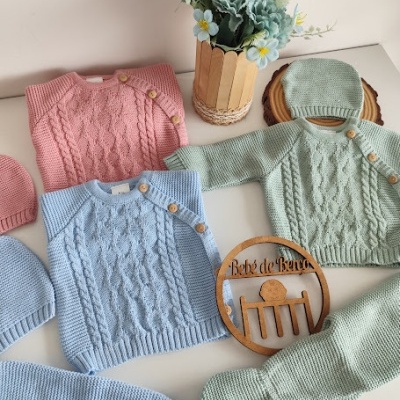 Roupas de bebé em tricô coloridas com botões, vaso de flores e placa de madeira Bebé de Berço