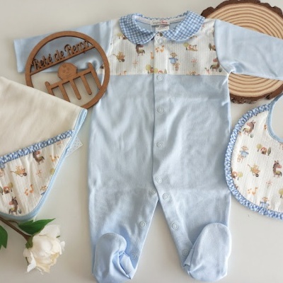 Conjunto de roupa de bebé azul e creme com macacão, babete e manta, decorado com padrão de animais, sobre fundo branco com elementos em madeira