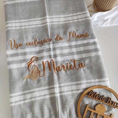 Toalha cinza com riscas brancas, bordado laranja com texto e imagem, máscara branca e decoração de madeira