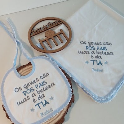 Babete e toalha bordados com texto em azul sobre superfície branca e base de madeira