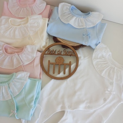 Conjunto de macacões de bebé com gola babado em várias cores claras e placa decorativa em madeira com texto
