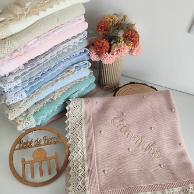 Mantas de bebé coloridas com bordas de renda e texto bordado, vaso com flores e placa de madeira