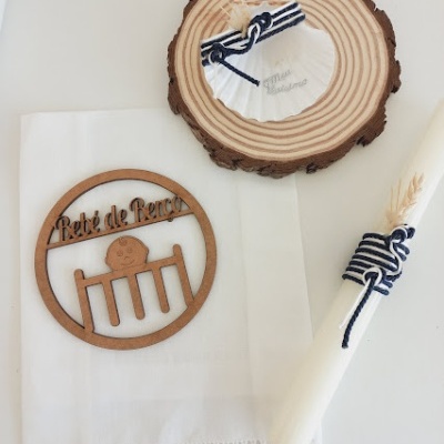 Conjunto eucarístico com toalha branca, castiçal branco e ornamento de madeira com texto e desenho, numa base de madeira redonda