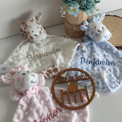 Três mantas de bebé com nomes bordados, cabeça de girafa como parte do design, flor azul artificial em vaso e decoração de madeira gravada.